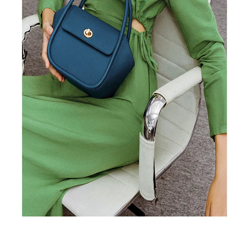 A wing-shaped women's leather tote bag with a buckle latch, shown in blue with a cross-body strap.