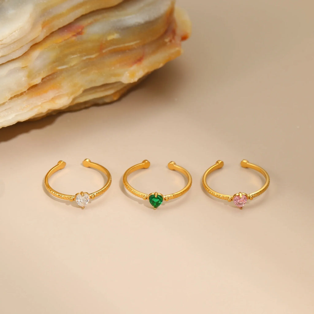 Open-ended adjustable ring with heart-shaped zircon decoration in geometric styling, shown in three colour variations.
