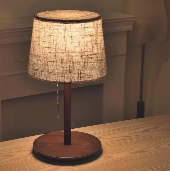 Walnut coloured solid wood bedside lamp with fabric shade on wooden surface