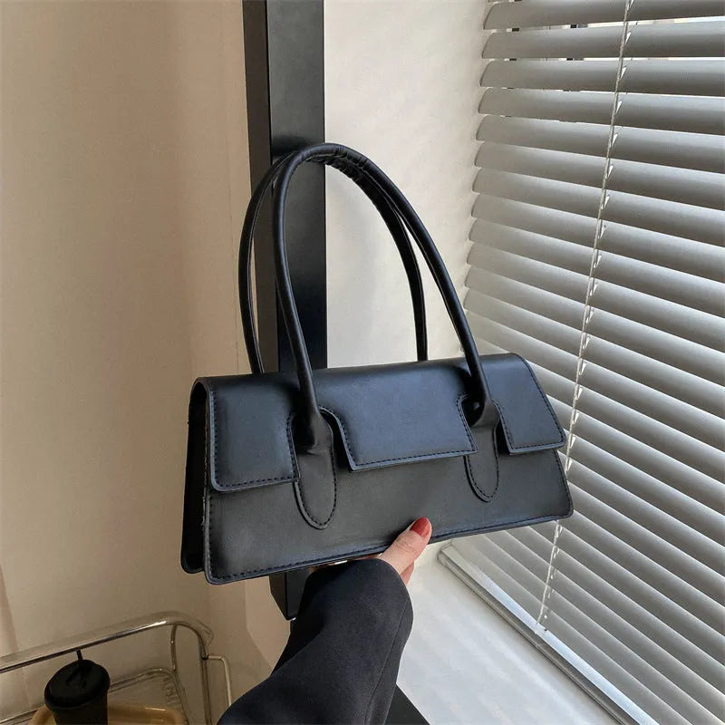 Women's black PU leather small square shoulder bag with stitching detail on a table.