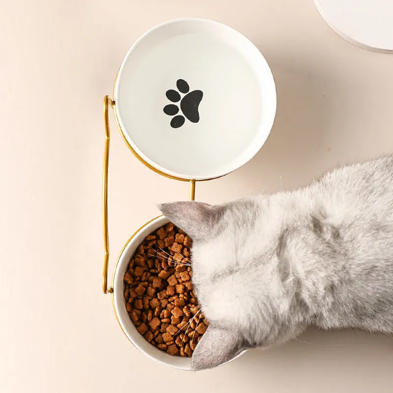 White ceramic cat bowl with cat paw print design on a black iron stand, shown as a pet feeding station.