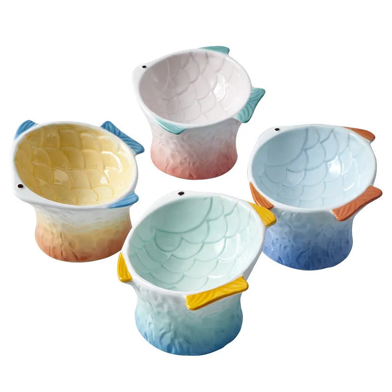 Four coloured fish-shaped ceramic cat bowls with tilted bases on a table.