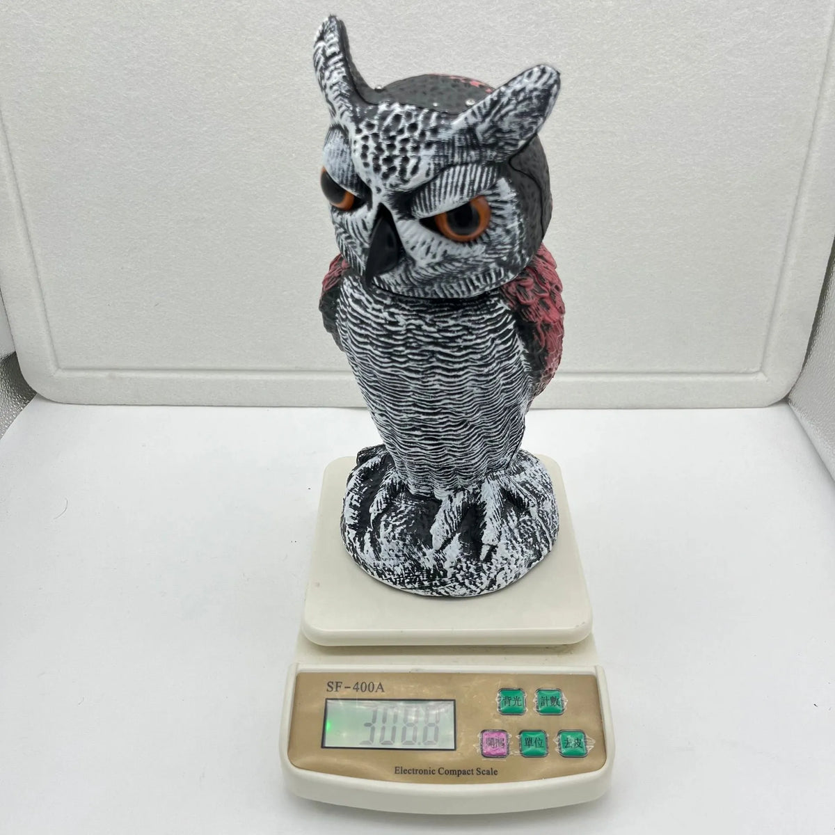 Polyethylene artificial owl bird scarer ornament with moving head, shown in a garden setting.