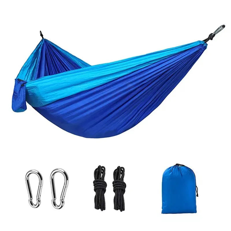 Blue outdoor camping hammock made from parachute nylon fabric, hanging between two trees.