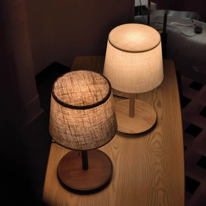 Walnut coloured solid wood bedside lamp with fabric shade on wooden surface