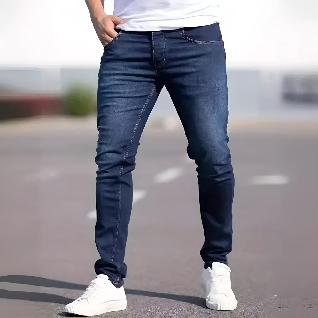 Man wearing dark blue slim-fit skinny jeans with a zipper fly, showcasing the mid-waist and street fashion style.