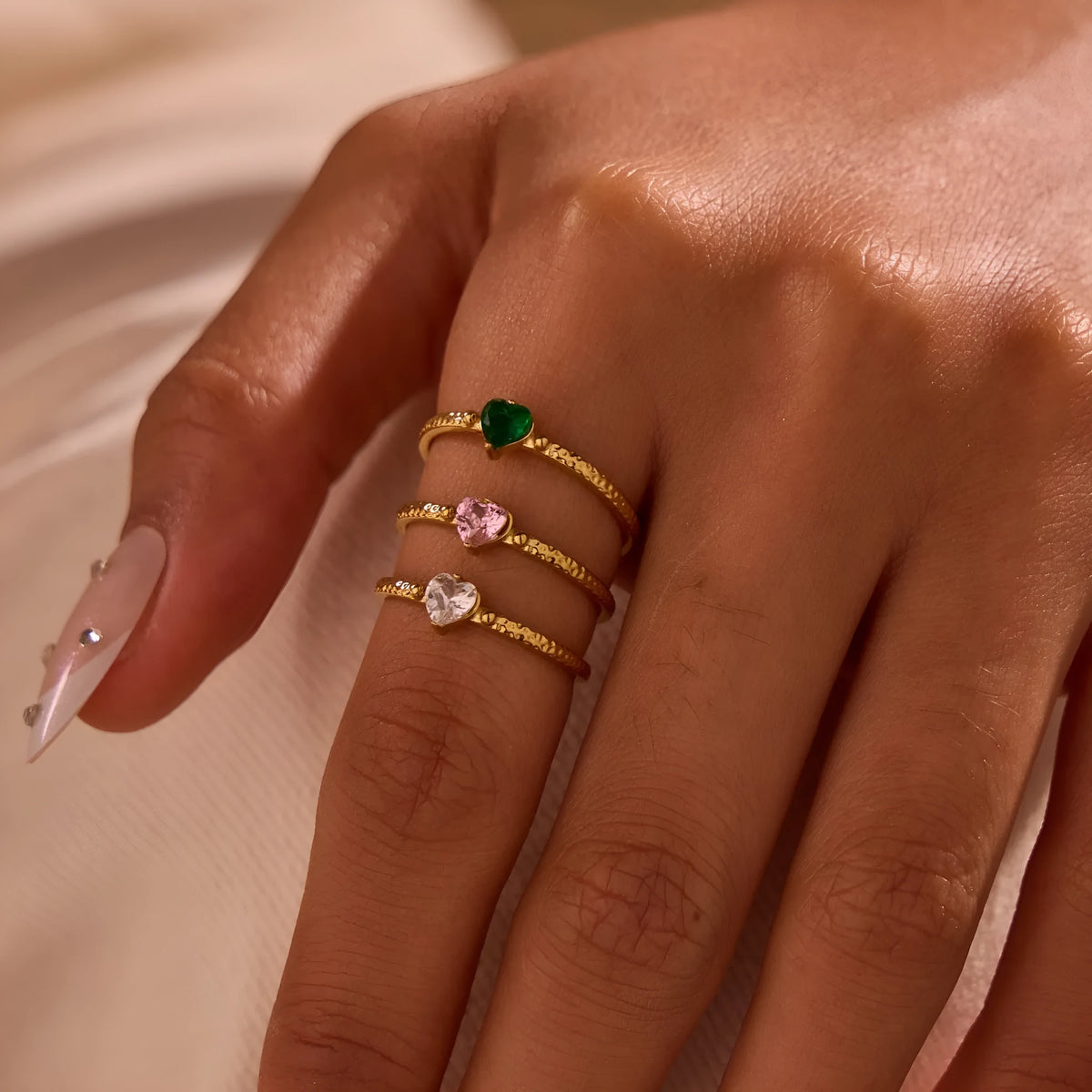 Open-ended adjustable ring with heart-shaped zircon decoration in geometric styling, shown in three colour variations.