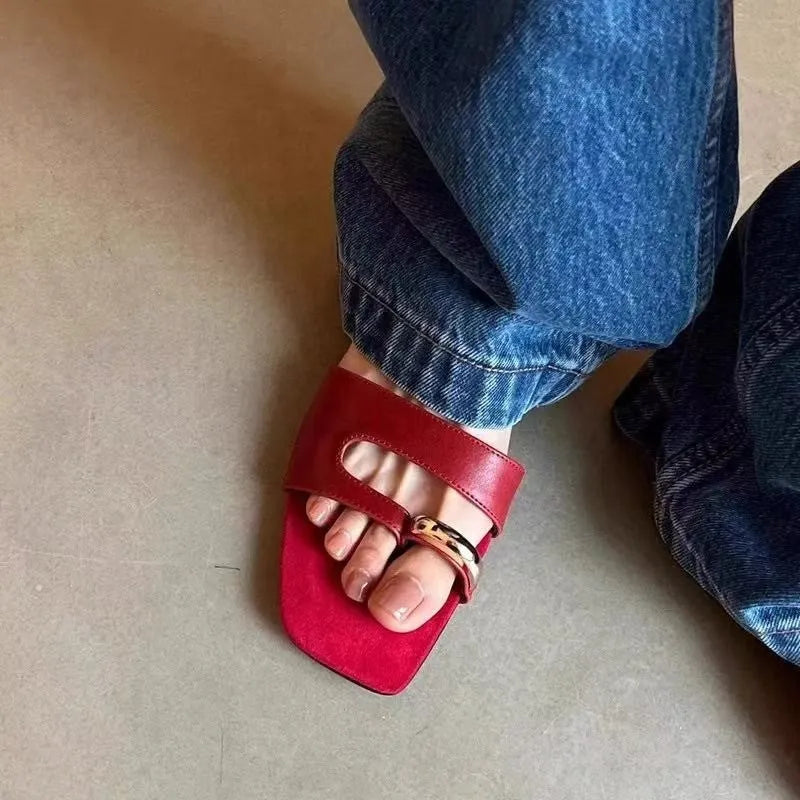 A pair of black square-toe slippers with a leather upper and light rubber sole on a wooden floor.