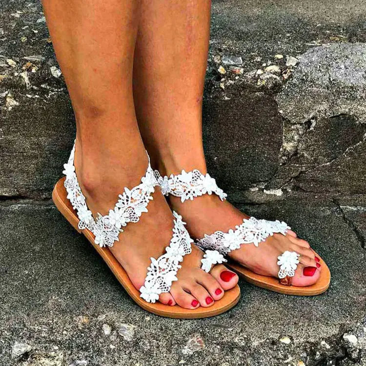 White women's flat sandals with rhinestone flower decoration on patent leather upper, showing round toe and slip-on design