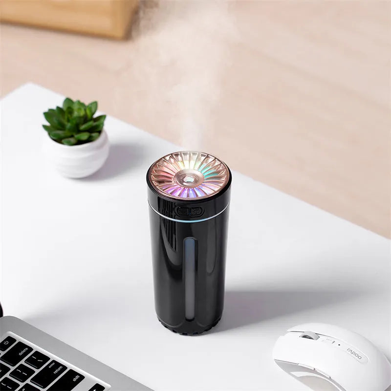 Black wireless ultrasonic humidifier with colourful lights, shown next to a USB cable on a desk.