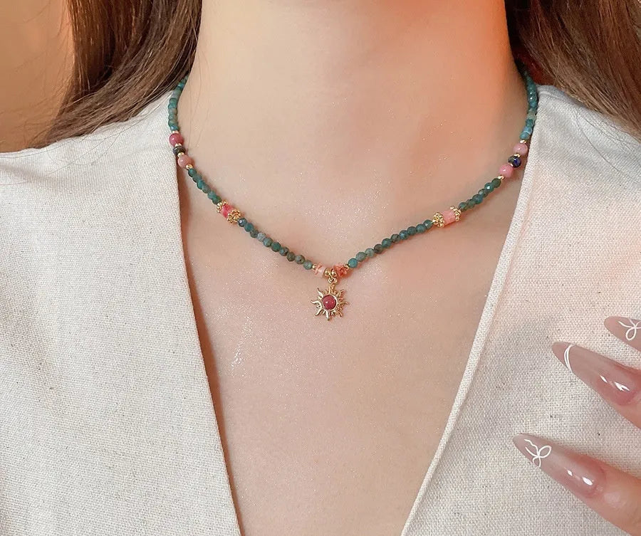 Stone sun pendant freshwater pearl necklace with gold blue pink chain on display.