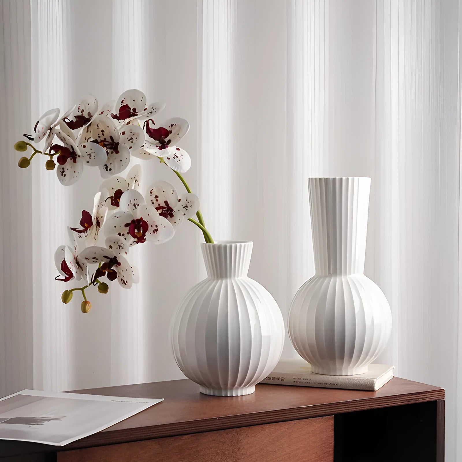 White ceramic ball vase with blue stripes and artificial orchid stems on wooden table.