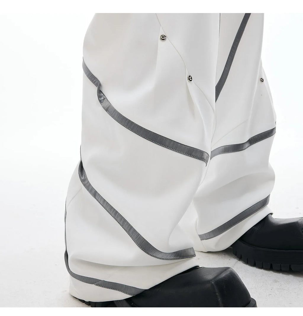 Men's black trousers with structured three-dimensional cut and metal rivet pleats on the legs.