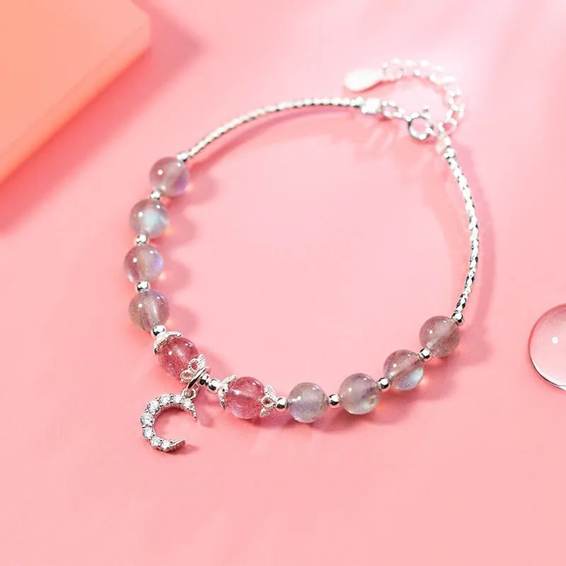 Handmade adjustable moonstone bracelet with a silver crescent moon charm and clear crystal accent on a grey background.