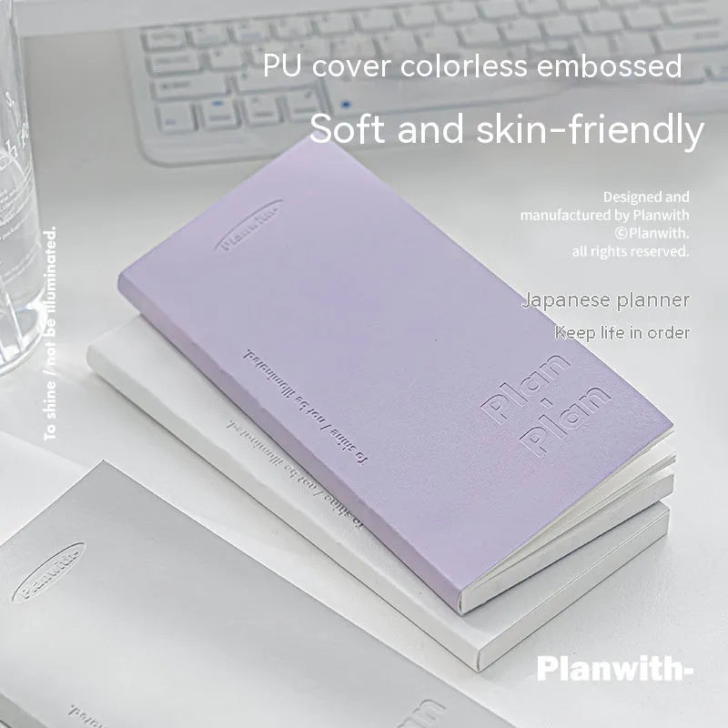 A5 embossed meter notebook open on a desk, showing white 100gsm paper and a choice of five cover colours.