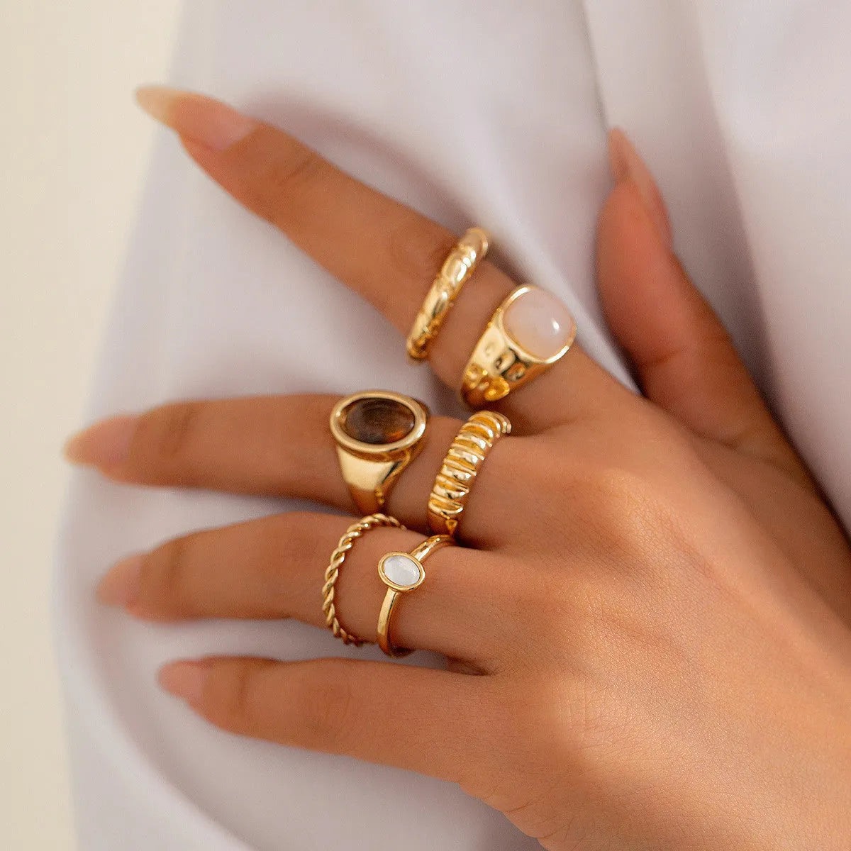 Six light gold alloy rings with geometric shapes and round elements arranged as a jewellery set