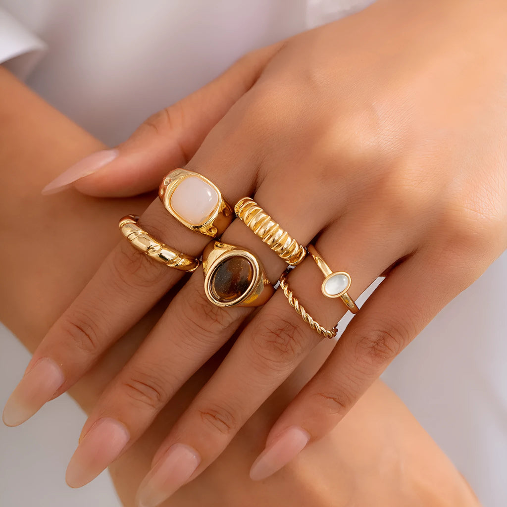 Six light gold alloy rings with geometric shapes and round elements arranged as a jewellery set