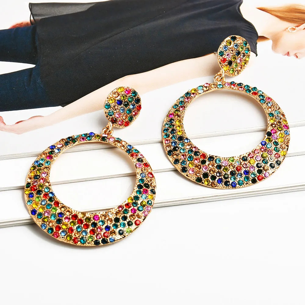 A pair of large, round, colour diamond-shaped cartoon-style metal pendant earrings on a white background.