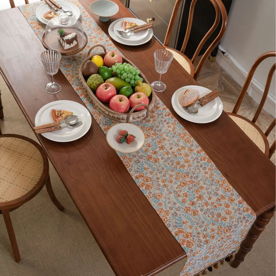 Beige jacquard table runner with long tassels and floral pattern laid on a wooden table