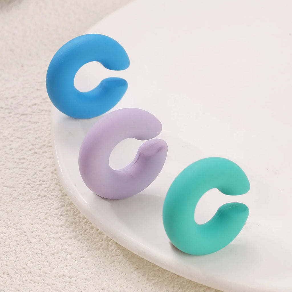 Geometric C-shaped matte clip-on earrings in multiple candy colours on a white background.