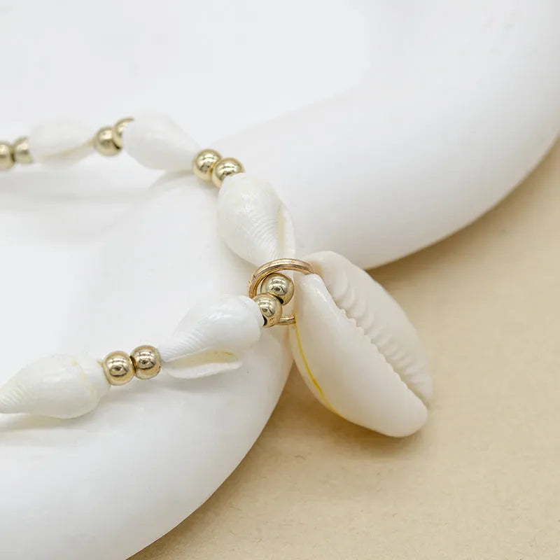 White necklace with a mother of pearl conch shell pendant and beads on an electroplated chain.