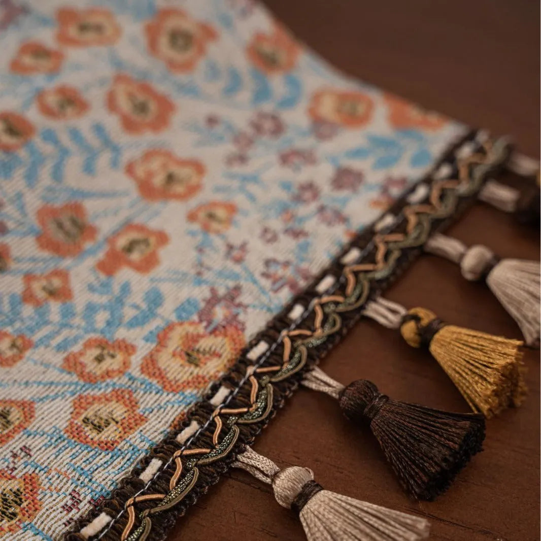 Beige jacquard table runner with long tassels and floral pattern laid on a wooden table