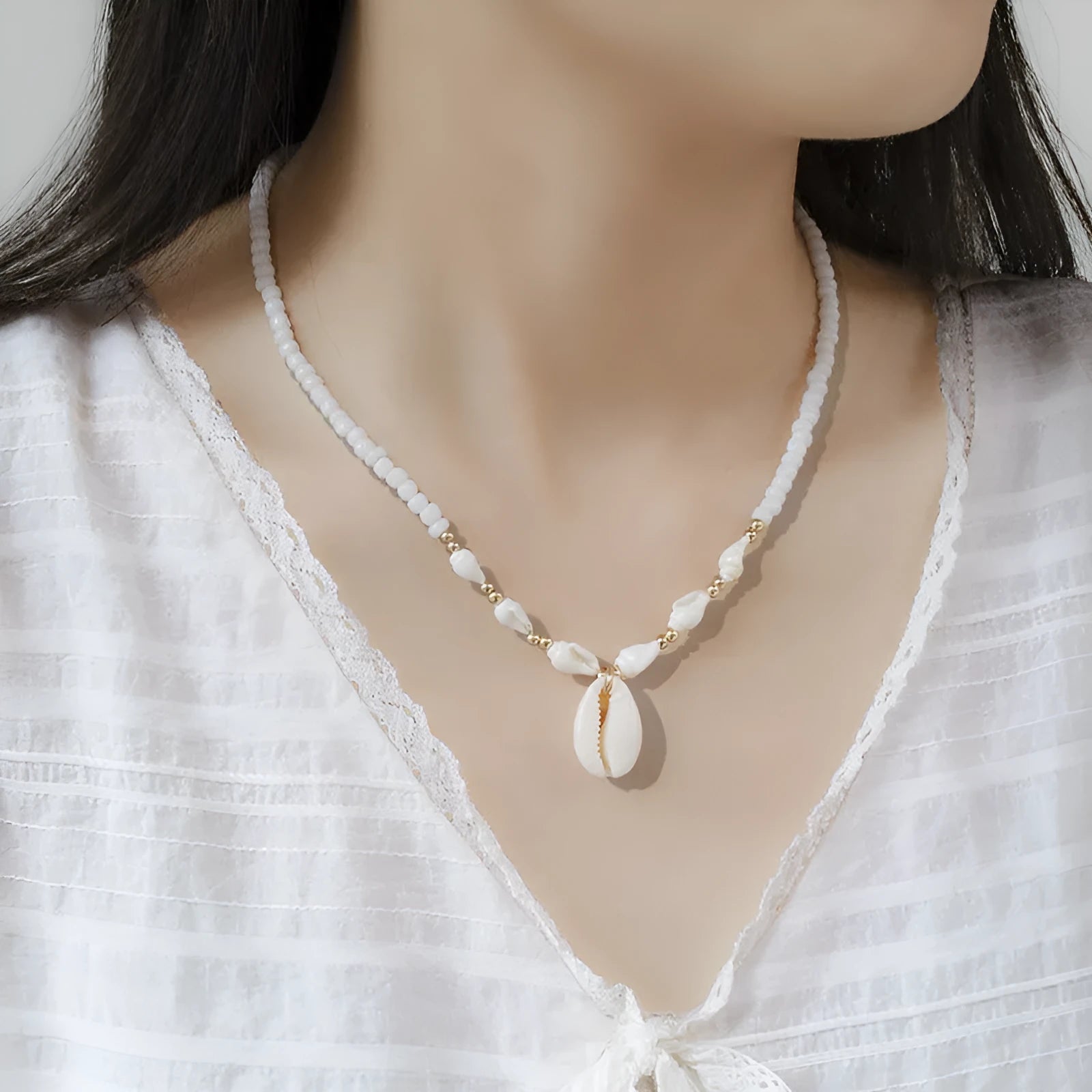 White necklace with a mother of pearl conch shell pendant and beads on an electroplated chain.