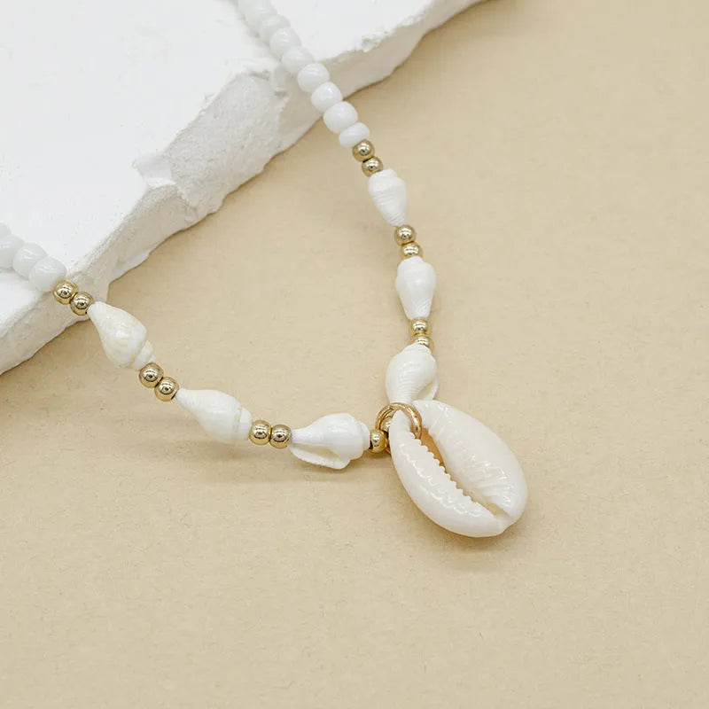 White necklace with a mother of pearl conch shell pendant and beads on an electroplated chain.
