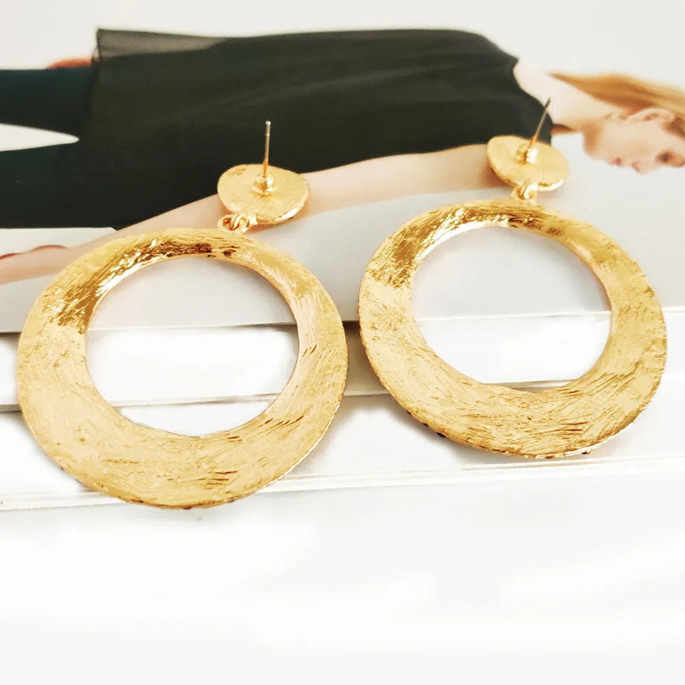 A pair of large, round, colour diamond-shaped cartoon-style metal pendant earrings on a white background.