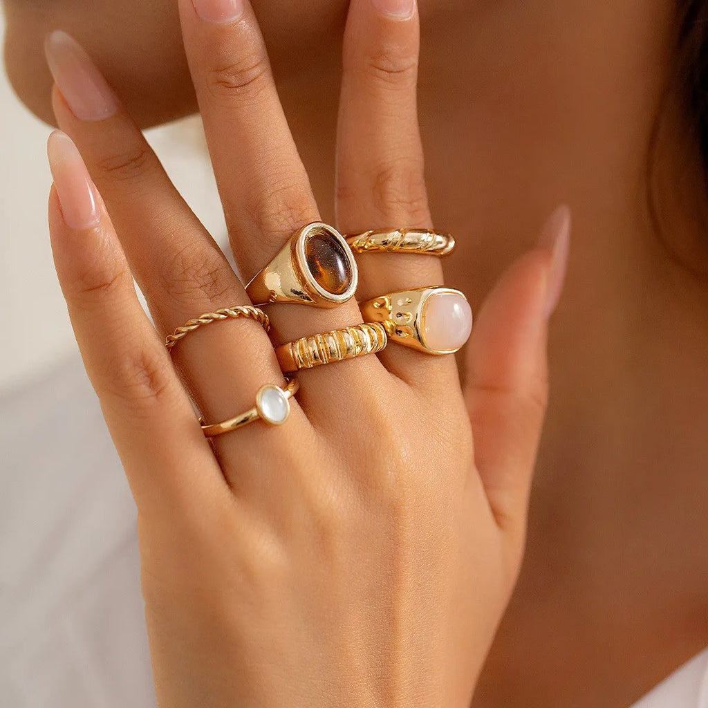 Six light gold alloy rings with geometric shapes and round elements arranged as a jewellery set