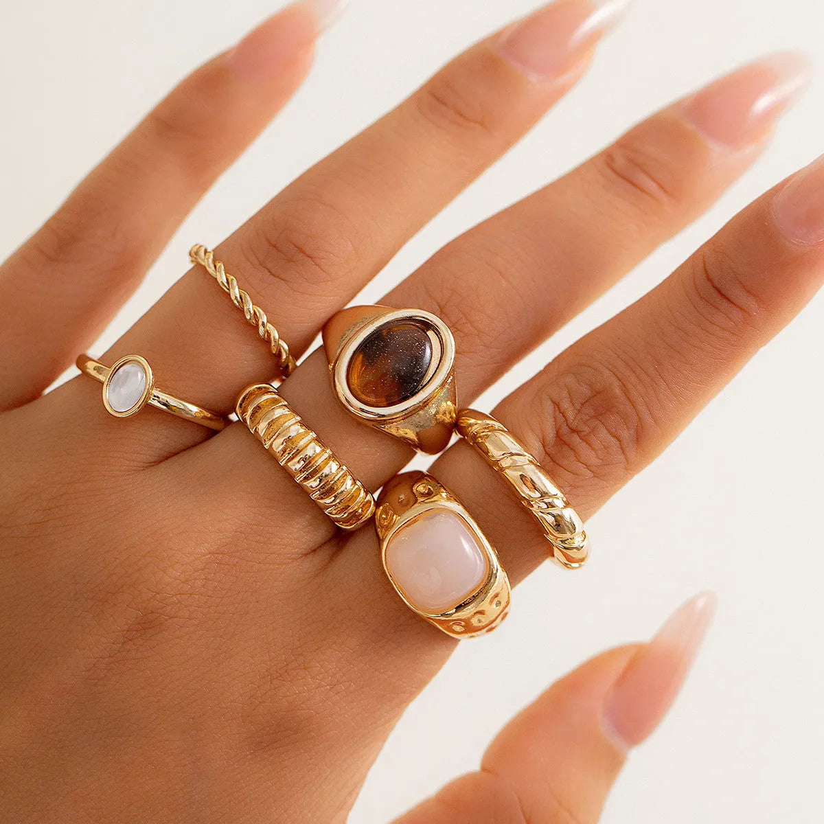 Six light gold alloy rings with geometric shapes and round elements arranged as a jewellery set