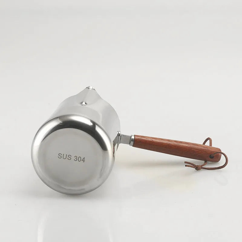 Stainless steel milk pouring cup with wooden handle and interior volume measurement scale.