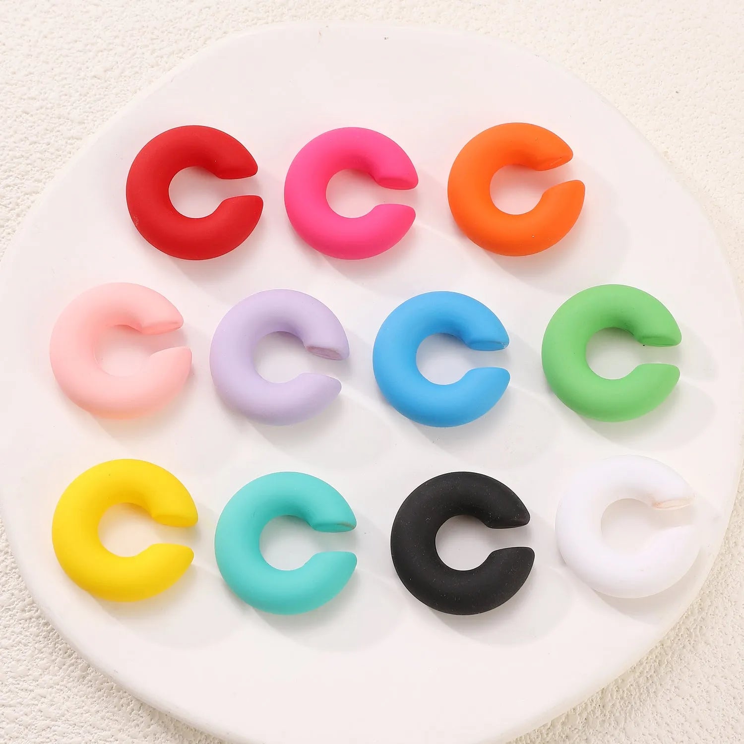 Geometric C-shaped matte clip-on earrings in multiple candy colours on a white background.