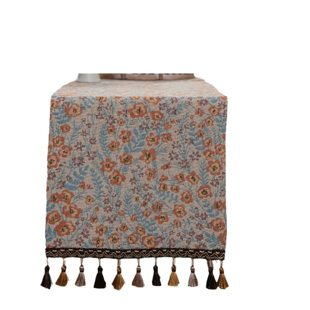 Beige jacquard table runner with long tassels and floral pattern laid on a wooden table