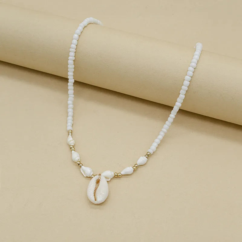 White necklace with a mother of pearl conch shell pendant and beads on an electroplated chain.