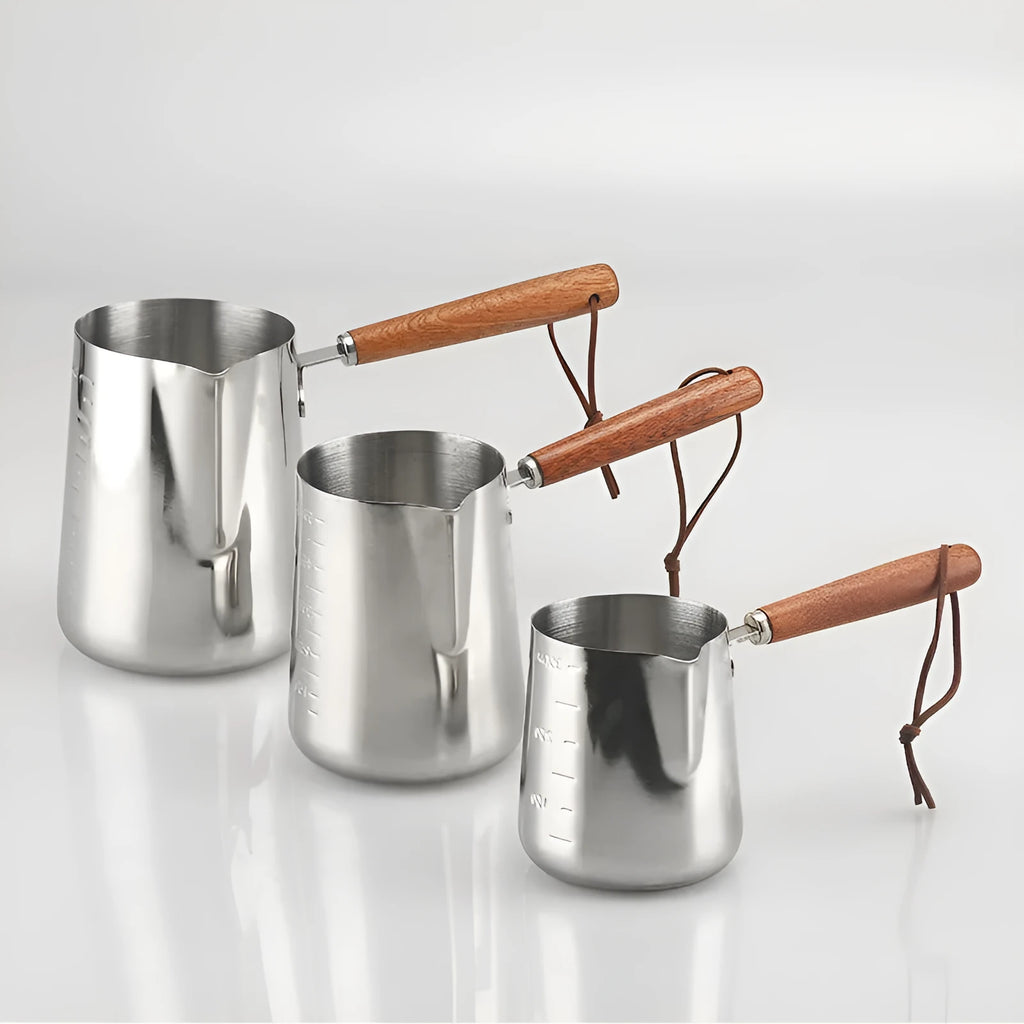 Stainless steel milk pouring cup with wooden handle and interior volume measurement scale.