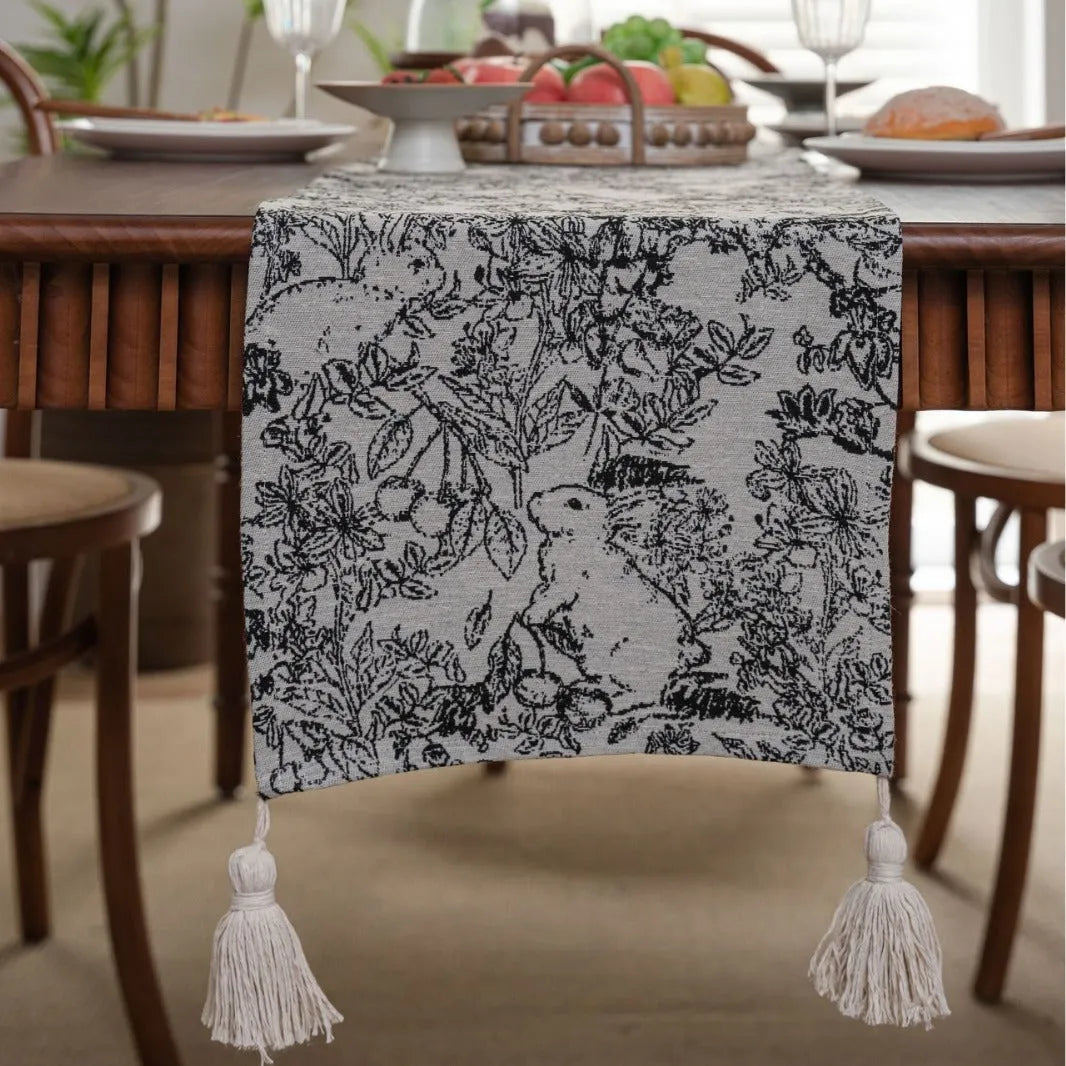 Beige jacquard table runner with long tassels and floral pattern laid on a wooden table