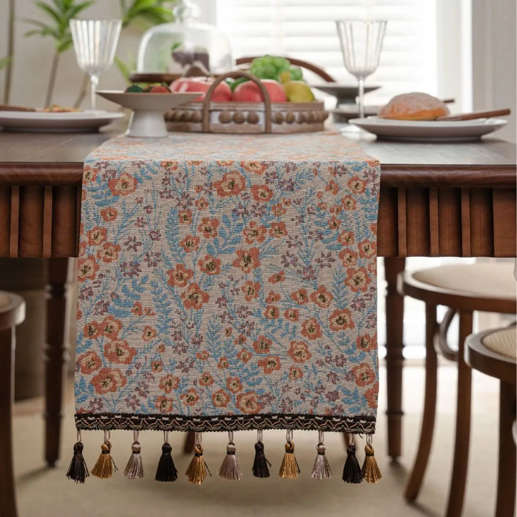 Beige jacquard table runner with long tassels and floral pattern laid on a wooden table