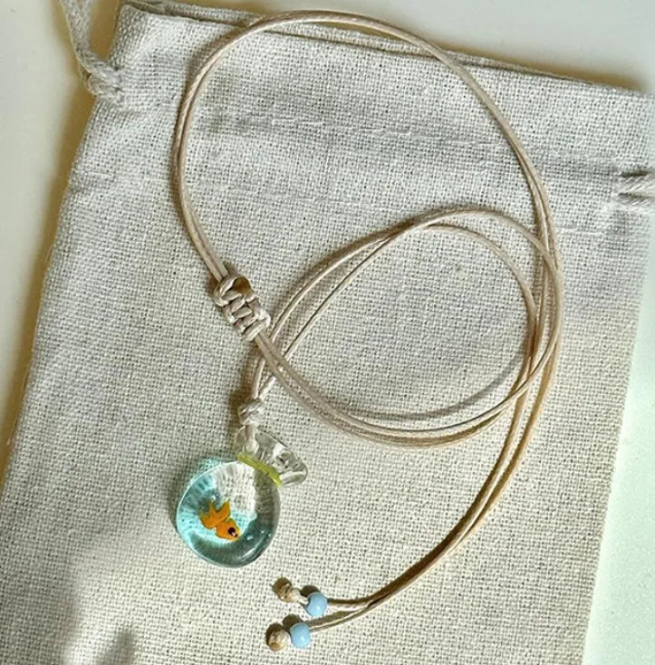 Women's necklace with small coloured glaze fish lucky bag pendant on a braided cotton and linen chain.