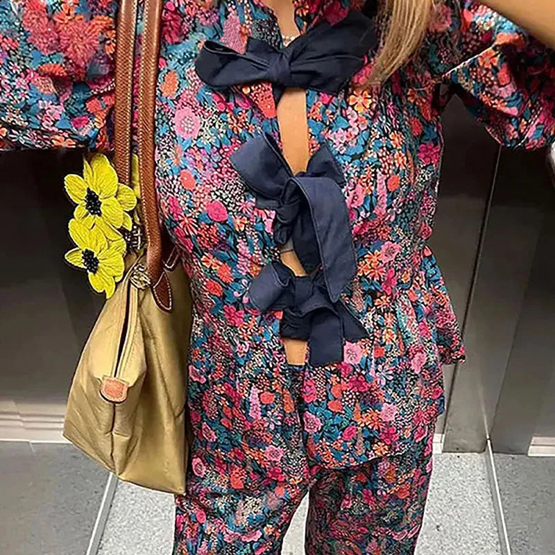 Women's floral print trouser suit set featuring a tie-neck blouse with puff sleeves and matching trousers.
