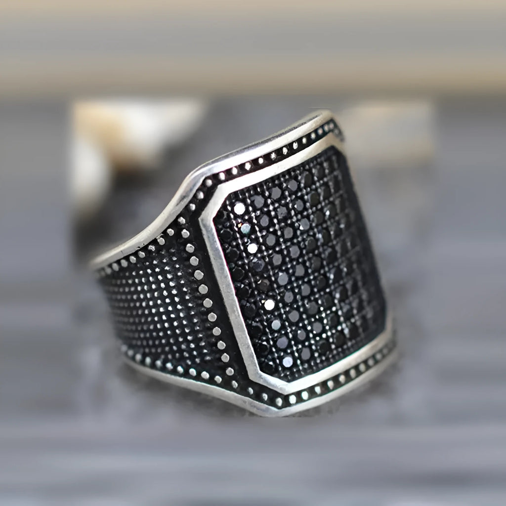Black alloy ring with copper inlaid detail around a central zircon stone.