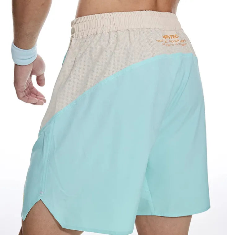 Men's loose grey workout shorts with elastic waist and lace-up fly on a gym floor.