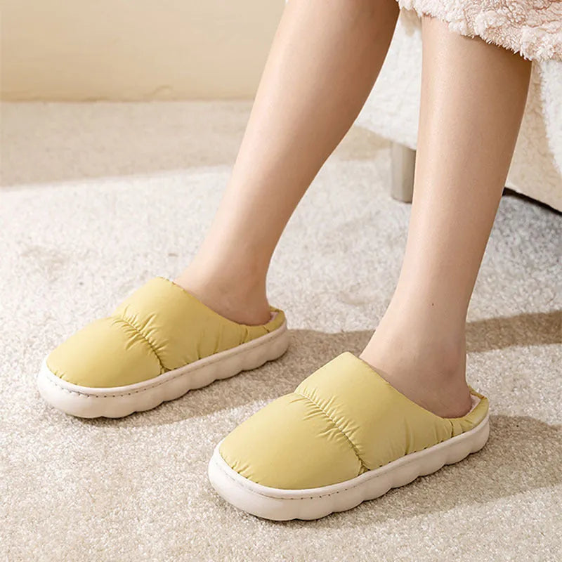 Pair of grey artificial leather slippers with a thick rubber sole and plush lining, shown on a wooden floor.
