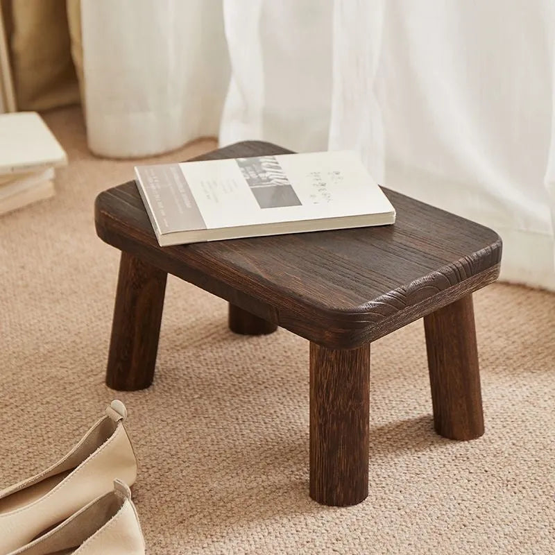 Solid wood changing stool with distressed finish and bracket legs in a living room setting.