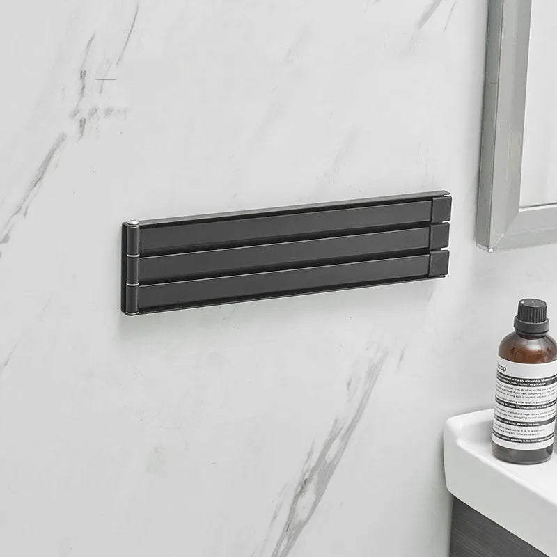 Black folding towel rack mounted on a bathroom wall with towels hanging, showing its no-drill installation.