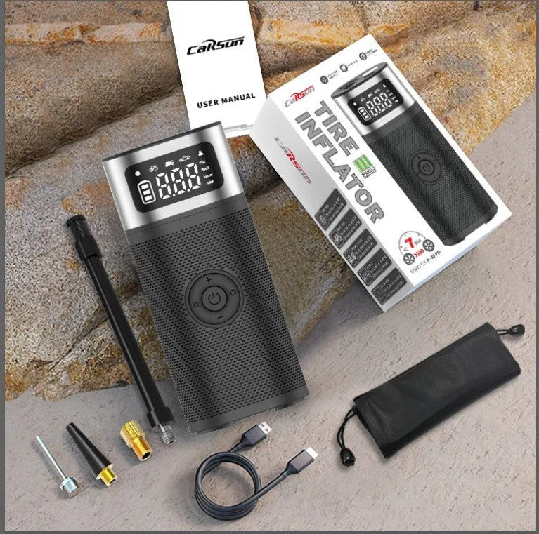 Black portable wireless air pump with digital display, LED light, and attached inflation tube on a textured surface.