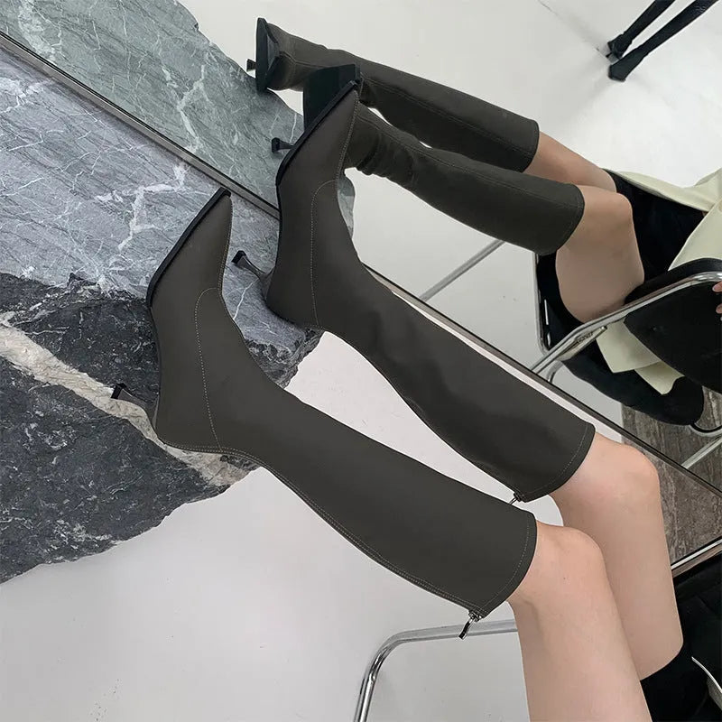 Black pointed toe below knee stiletto heel boots with a back zip, shown on a foot.