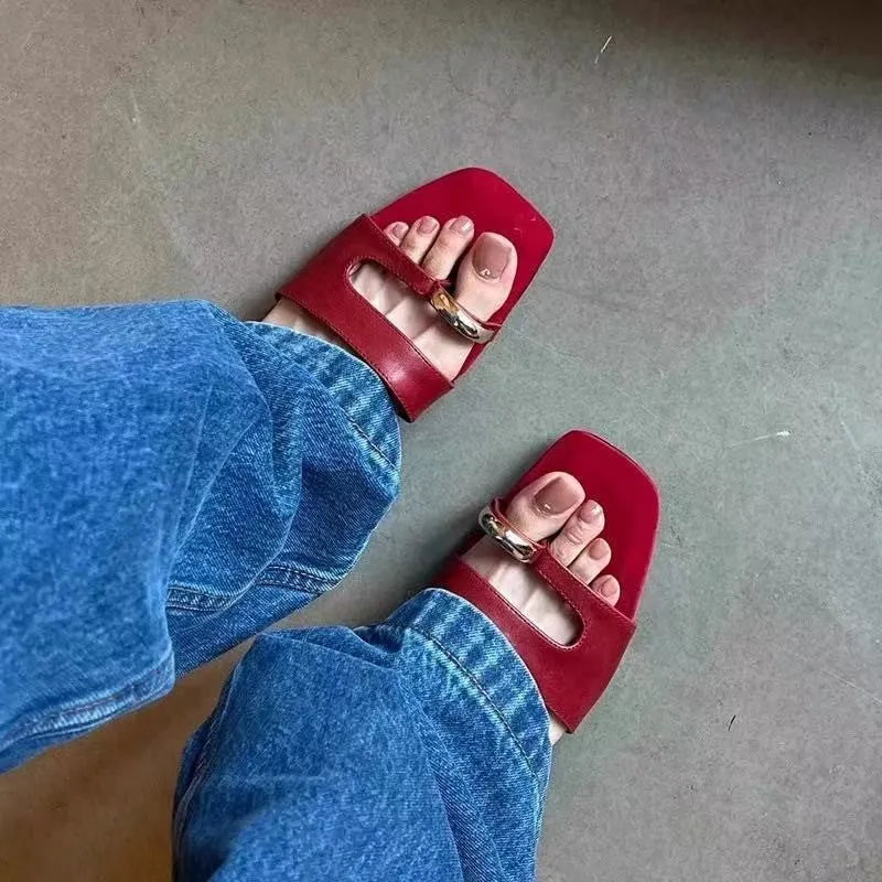 A pair of black square-toe slippers with a leather upper and light rubber sole on a wooden floor.