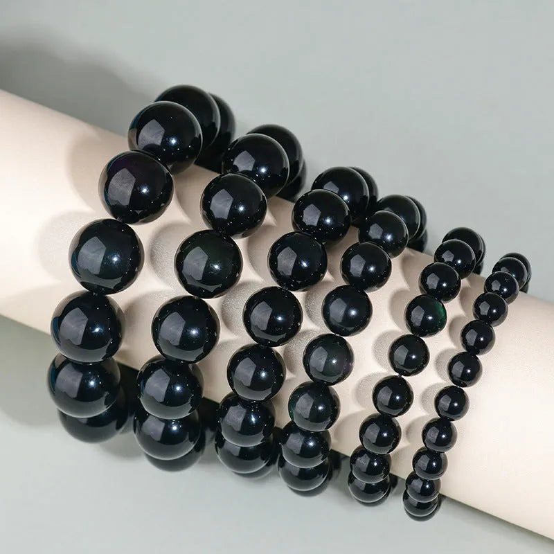 Hand-woven round obsidian bracelet in black stone, shown on a wrist.