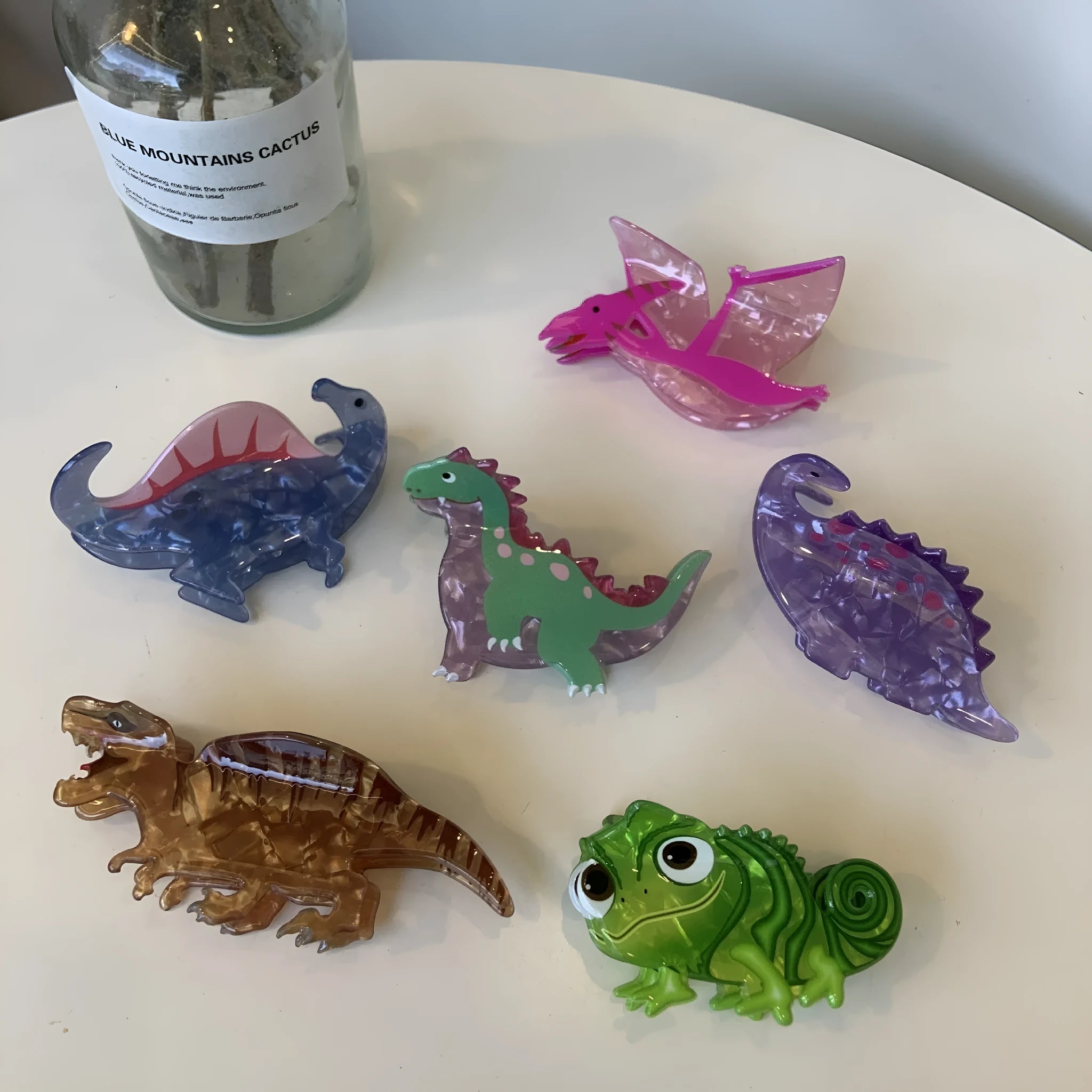 Dinosaur-shaped acrylic jaw clip hair grip in assorted colours including blue, brown, green, pink, and purple.